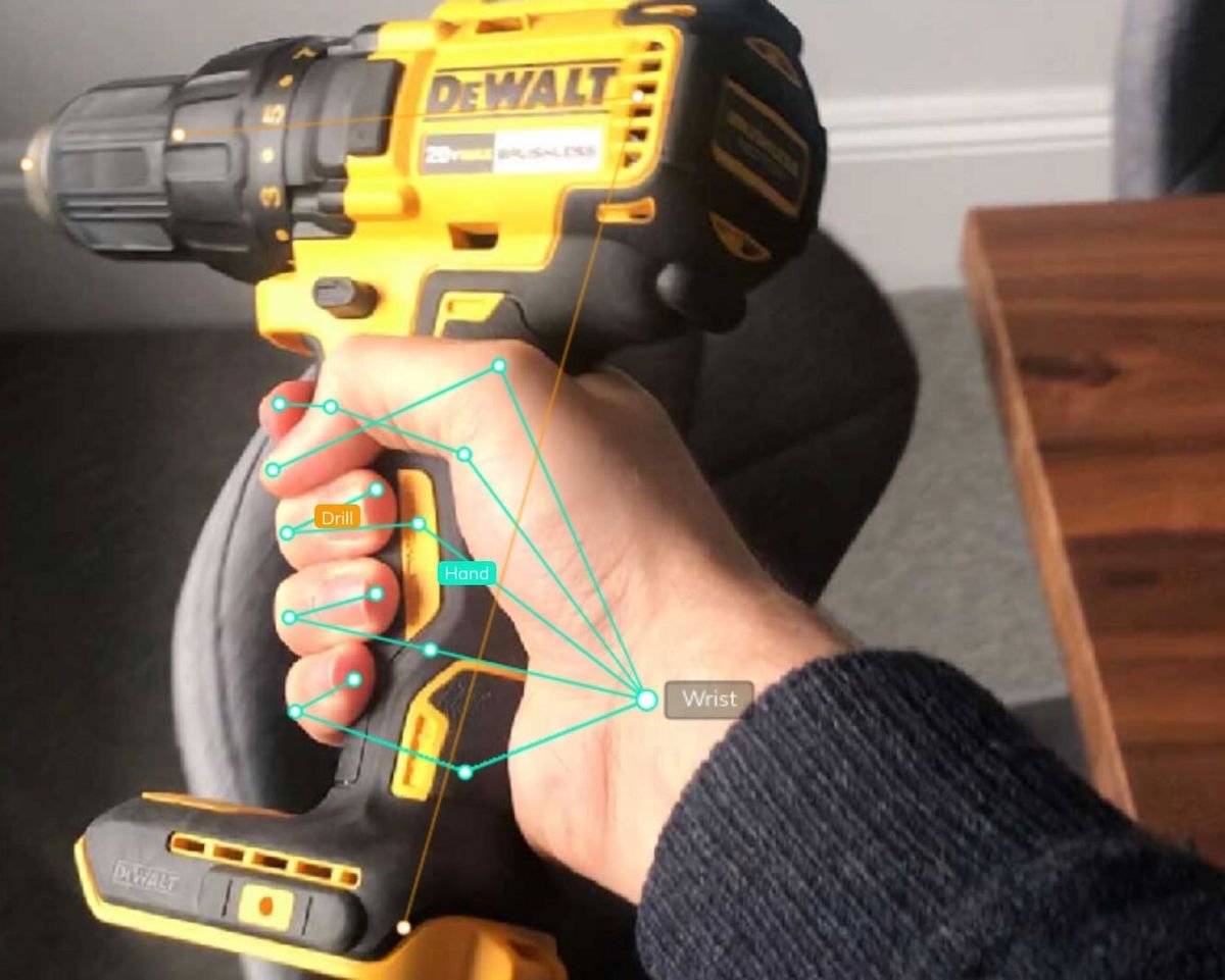 This is an example of image annotation for computer vision using a wireframe. The image shows a person’s right hand holding a cordless drilling tool, which is labeled with the word "drill." There are points that indicate the pose points of the person’s hand, with a point labeled "wrist," connecting to five other points to represent the position of the person’s fingers, which are labeled "fingers." Source: V7 Labs using Darwin, its data annotation tool.